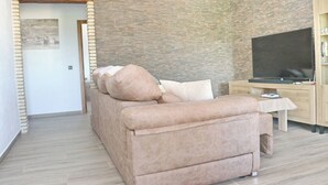 A modern living room with a beige sofa, a flat-screen TV, and a wooden entertainment unit. - Casa Marcucaña el Palmar (El Palmar)