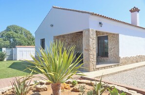 Un bâtiment blanc à la façade en pierre, doté d’un patio couvert et d’un jardin où poussent des agaves.