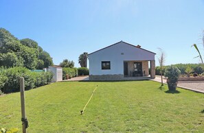 Une maison de plain-pied à l’extérieur blanc, avec un socle en pierre et un petit porche agrémenté d’une table et de chaises.