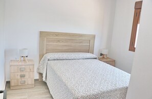 A bedroom with a wooden headboard, a bed with a floral bedspread, a bedside table with a lamp, and a wooden nightstand with a lamp. - Casa Marcucaña el Palmar (El Palmar)