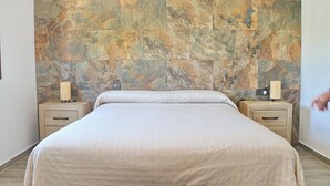 A bedroom with a stone-patterned headboard, a bed with a white bedspread, two bedside tables with lamps, and wooden nightstands. - Casa Marcucaña el Palmar (El Palmar)