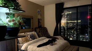 Un dormitorio con vista a la ciudad, una planta en maceta y un gato sobre la cama.