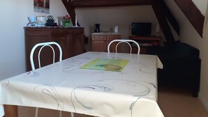 A dining area with a table set for two, a wooden cabinet, a television, and a staircase. - Villa Beauregard Furnished Appartment La Roche Posay (la roche posay)
