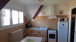 A compact kitchen with a dining table, a stove, a microwave, and a refrigerator. - Villa Beauregard Furnished Appartment La Roche Posay (la roche posay)