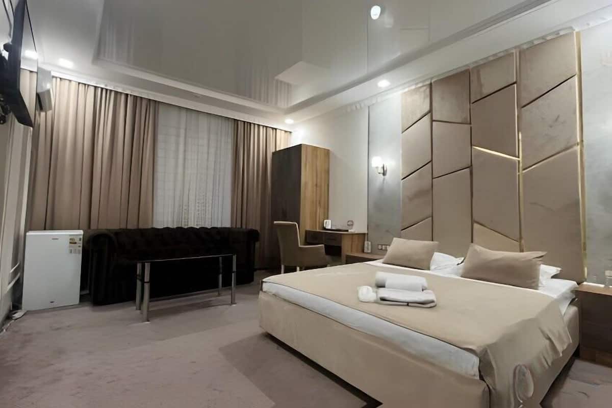 A modern hotel room with a large bed, a desk, a chair, and a wardrobe.