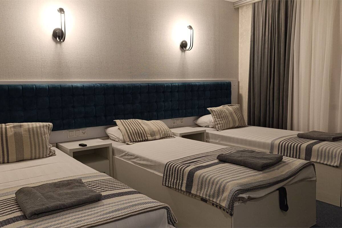 A hotel room with three single beds, each with a headboard, bedside tables, and lamps.
