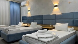A hotel room with two beds, each with white linens and pillows, a blue headboard, and wall-mounted lighting. - Sharq Hotel (Urgench)