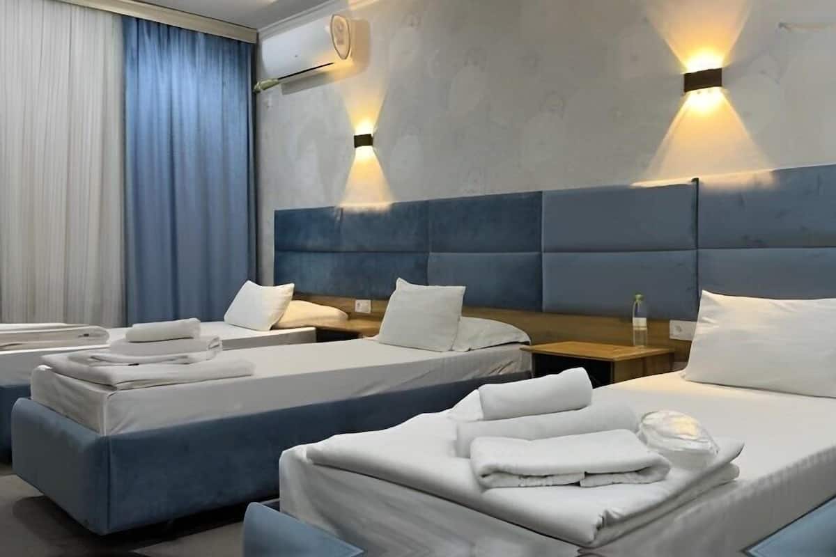 A hotel room with two beds, each with white linens and pillows, a blue headboard, and a nightstand with a bottle.