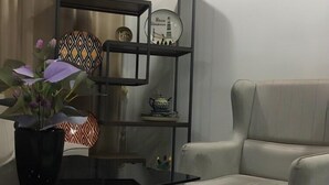A modern living room with a black glass table, a beige armchair, and a black shelving unit with decorative items. - Sharq Hotel (Urgench)