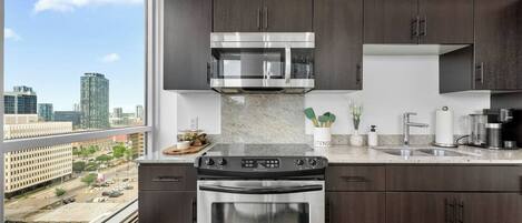 A modern kitchen with dark wood cabinets, stainless steel appliances, and a large window offering a city view.