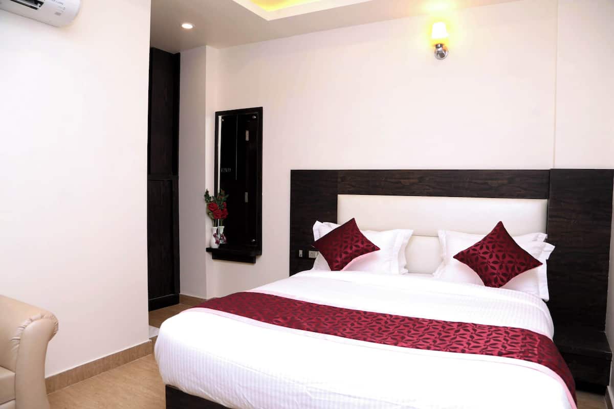 A hotel room with a large bed, a bedside table, a chair, a wall-mounted air conditioner, and a door.