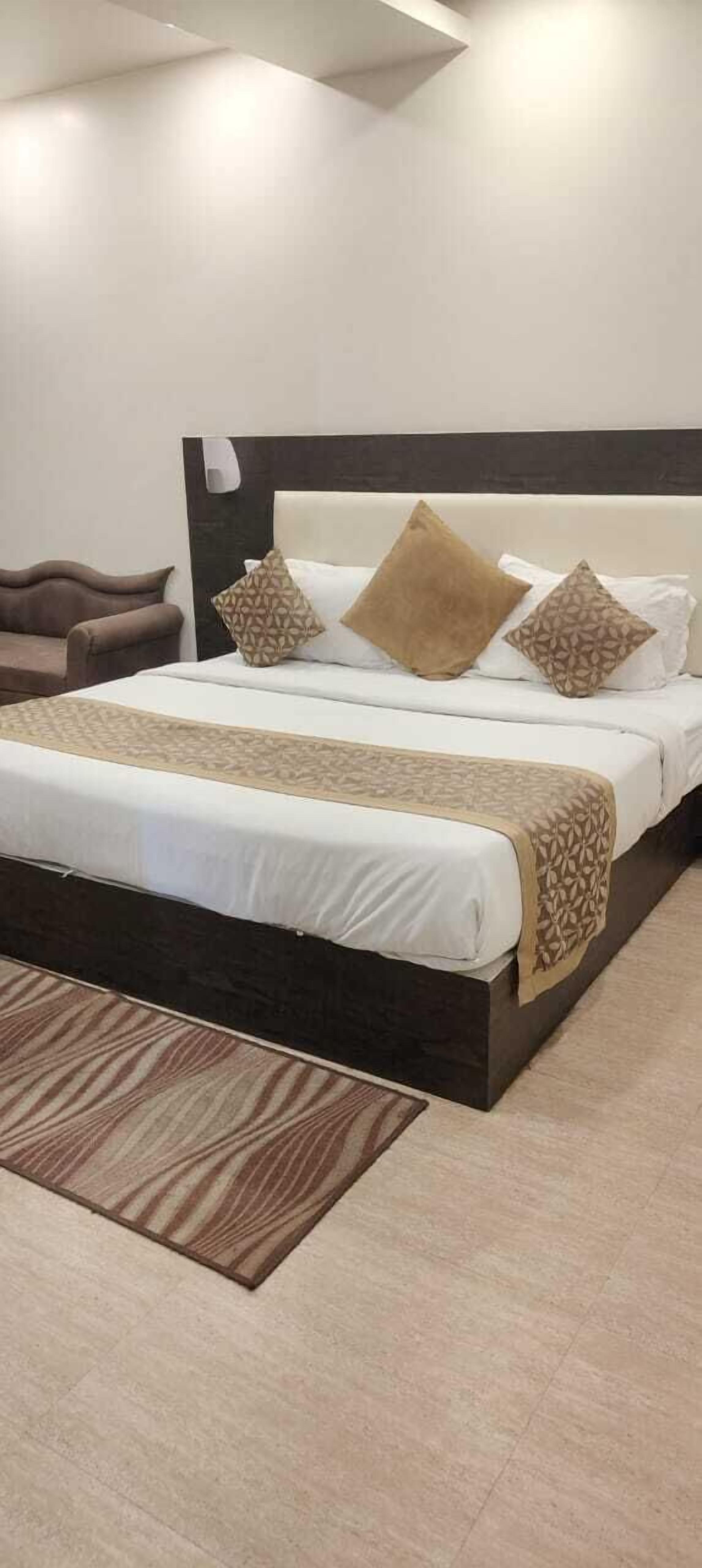 A modern hotel room with a large bed, dark headboard, and a patterned rug.