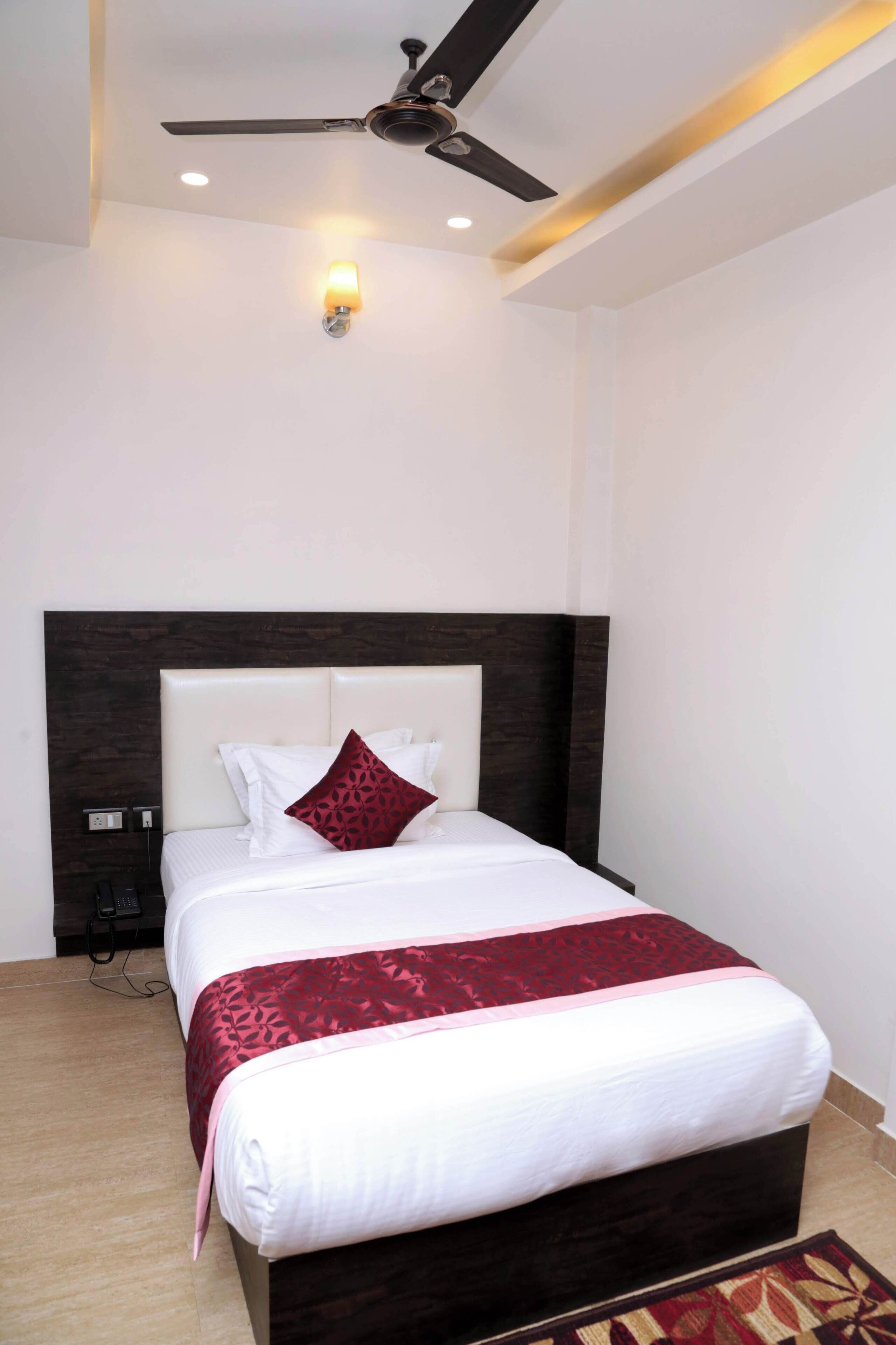 A neatly made bed with a dark headboard, a ceiling fan, and a wall-mounted light fixture.