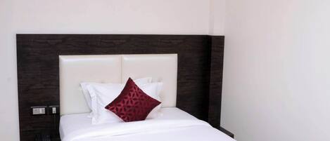 Una cama bien hecha con un cabecero oscuro, un ventilador de techo y una lámpara fijada a la pared.