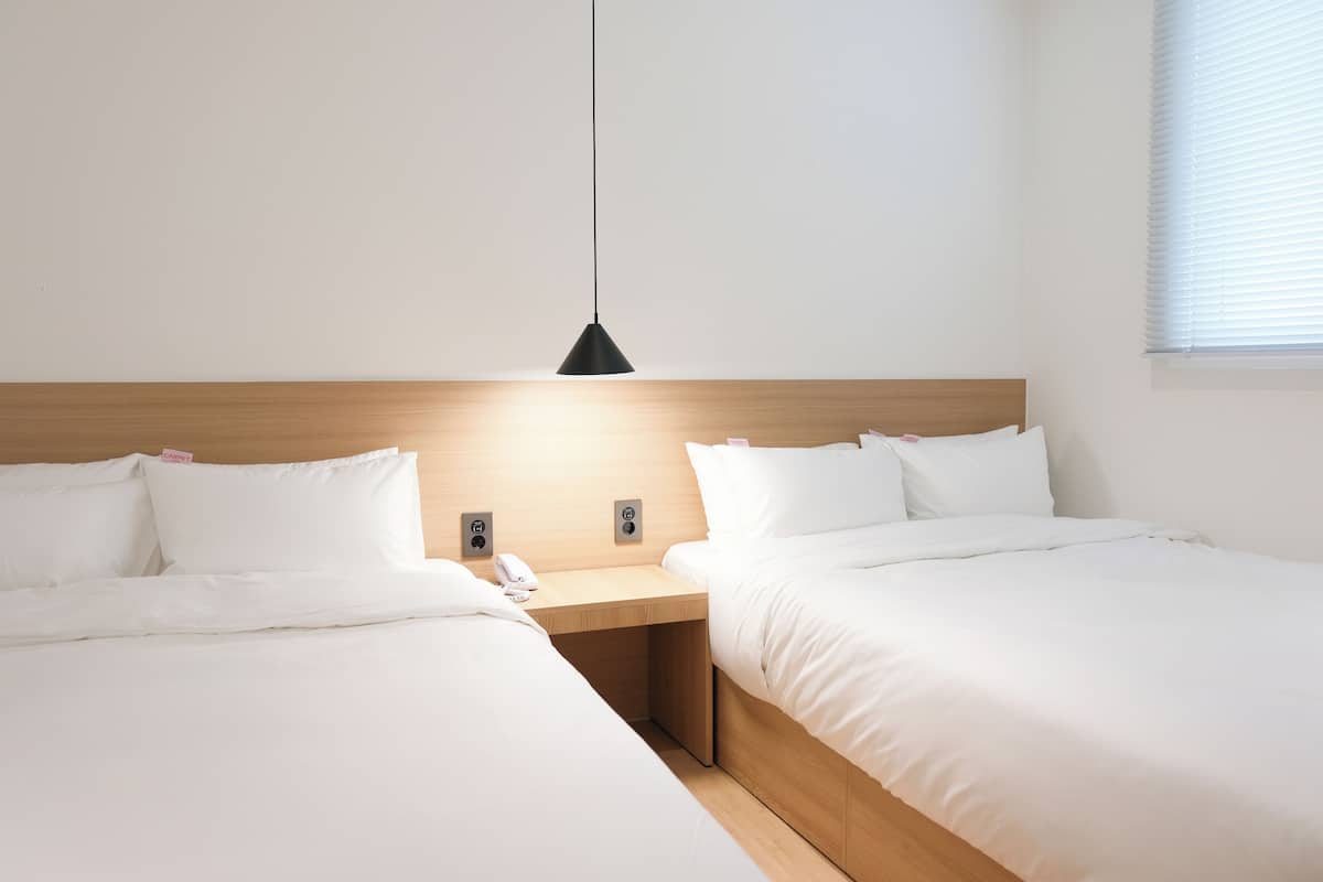A hotel room with two beds, a wooden headboard, a bedside table with a phone, and a hanging light fixture.