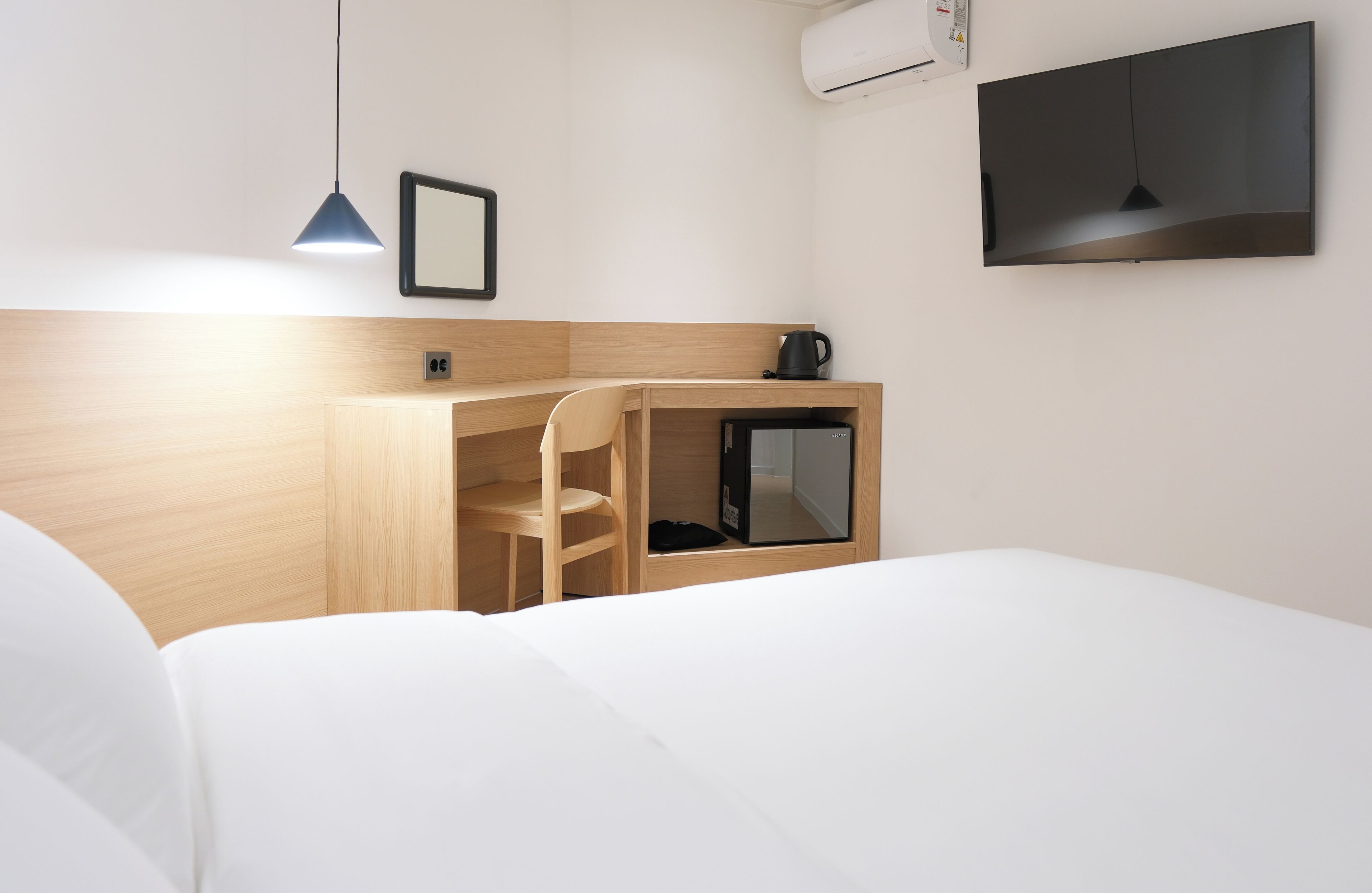 Habitación de hotel con cama, escritorio con silla, televisor y cafetera.