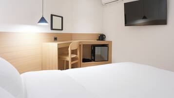 Habitación de hotel con cama, escritorio con silla, televisor y cafetera.