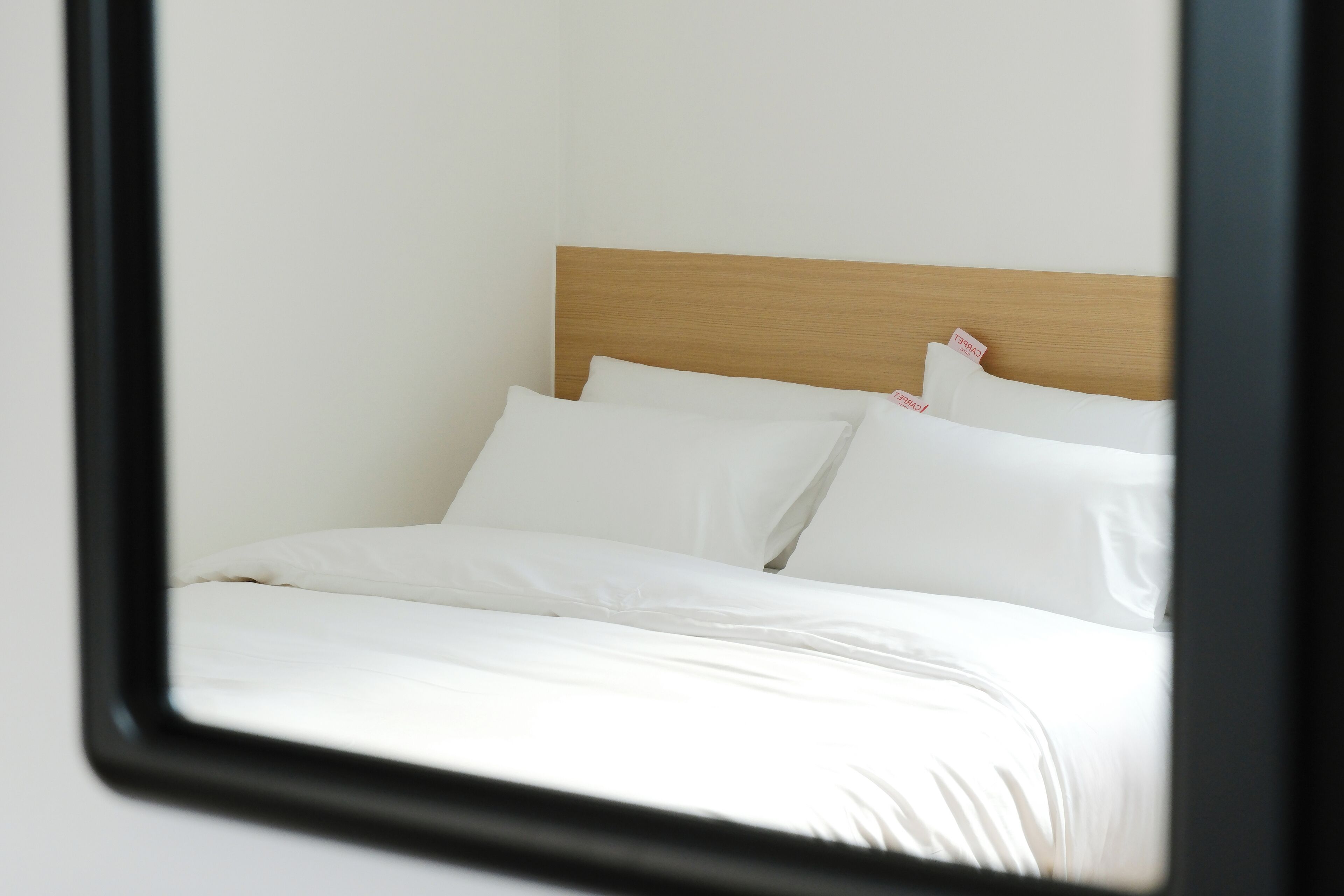 Ein ordentlich bezogenes Bett mit weißen Leinen und Kissen, ein Holz-Kopfteil und ein Spiegel, der das Bett reflektiert.