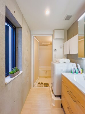 A narrow bathroom with a window, a built-in sink, a mirror, and a shower area. - ideas ASAKUSA (Tokyo)