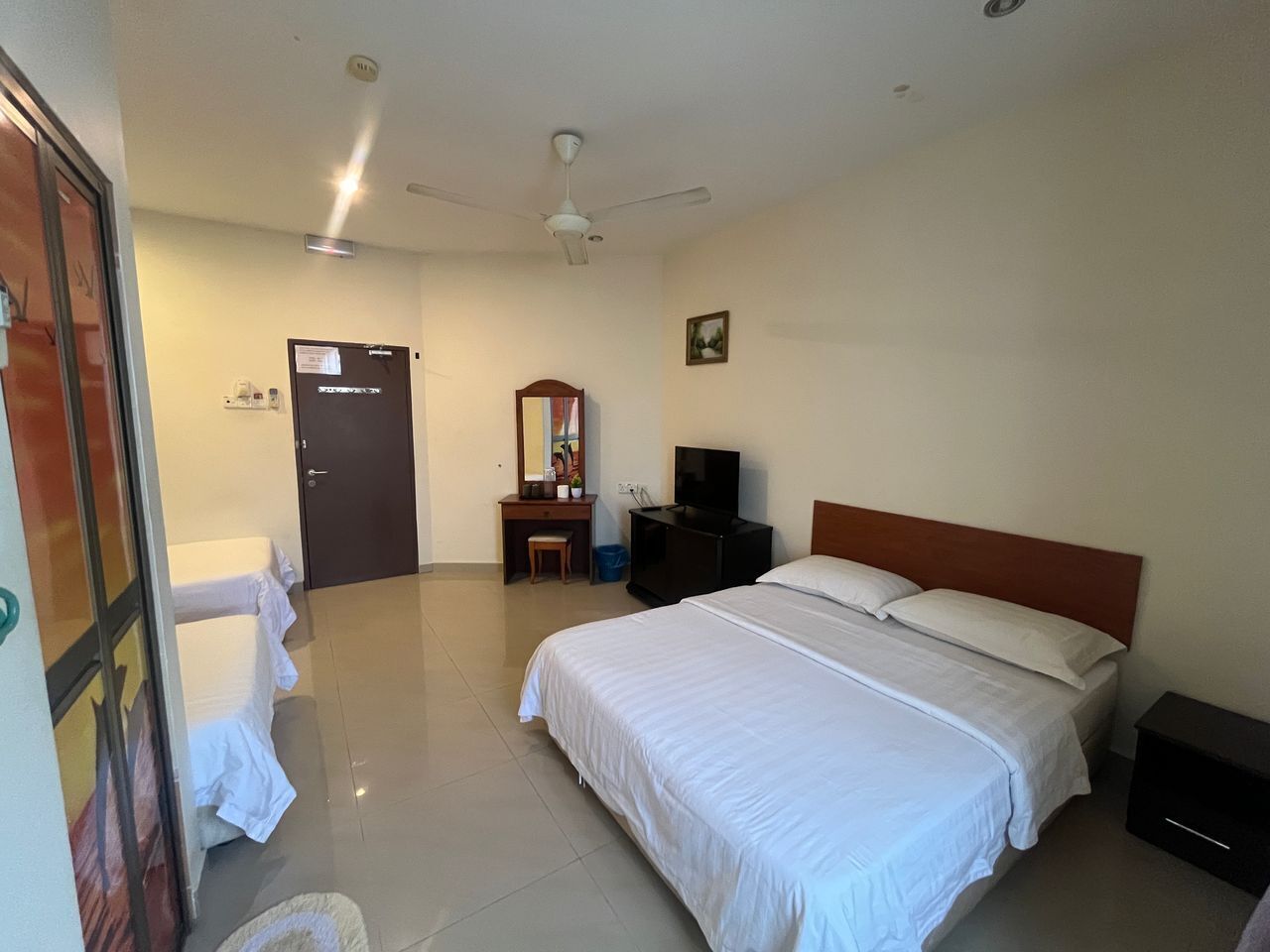 A hotel room with a large bed, a desk with a chair, a television, and a ceiling fan.