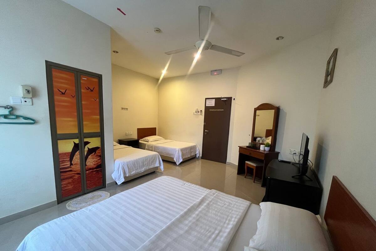 A hotel room with two single beds, a desk with a chair, a ceiling fan, and a door with a sign.