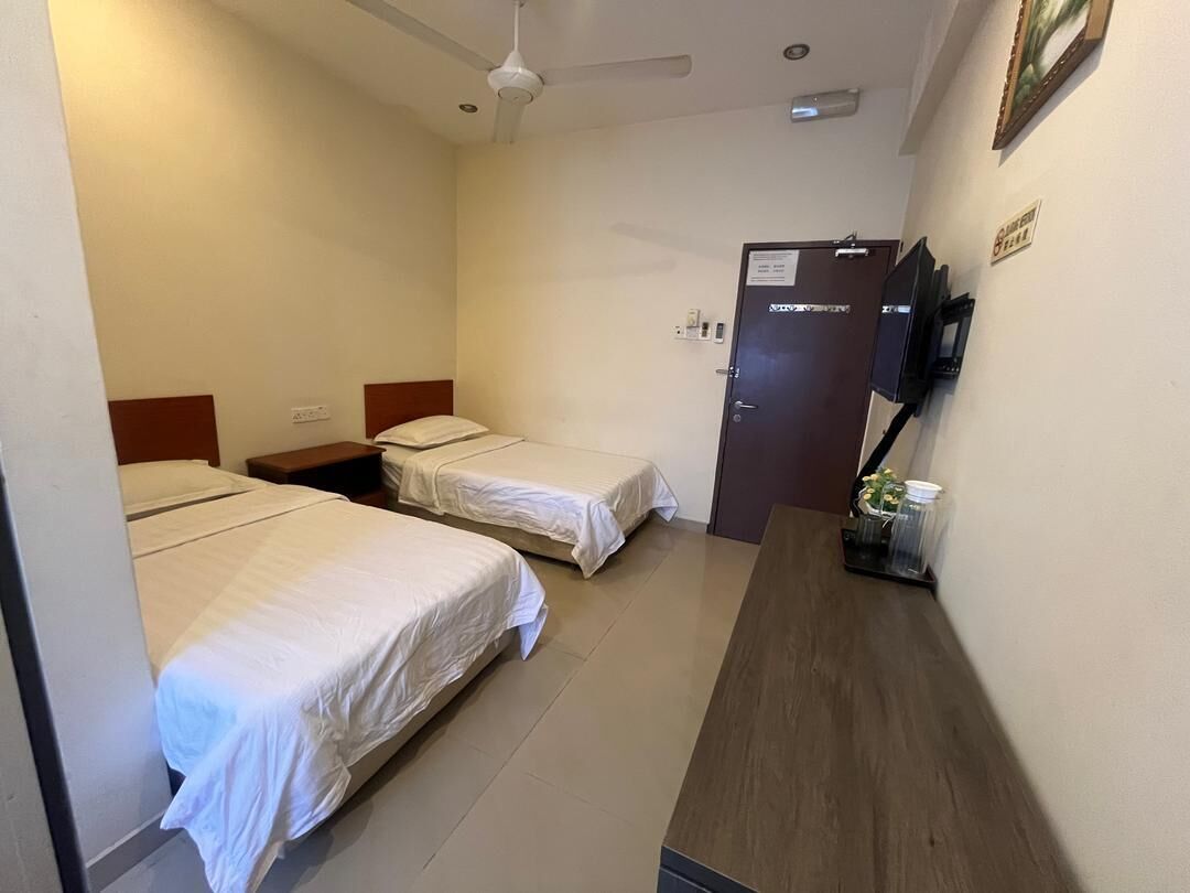 Habitación de hotel con dos camas individuales, un escritorio de madera, un ventilador de techo y una puerta con un letrero.
