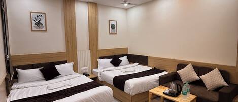 A modern hotel room with two beds, a sofa, a coffee table, and a ceiling fan.