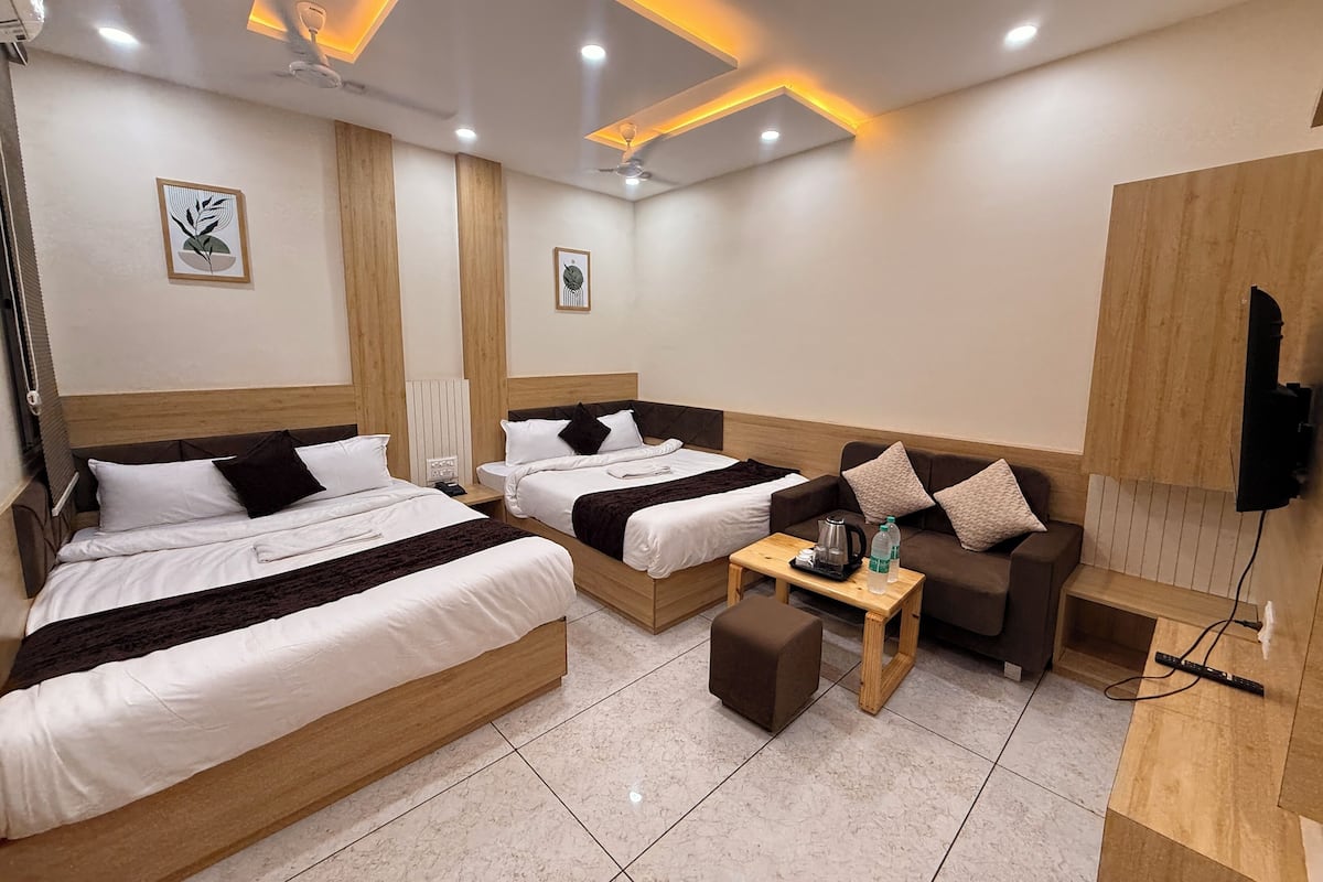 Quarto de hotel com duas camas, um sofá, uma mesa de centro e uma TV fixada na parede.