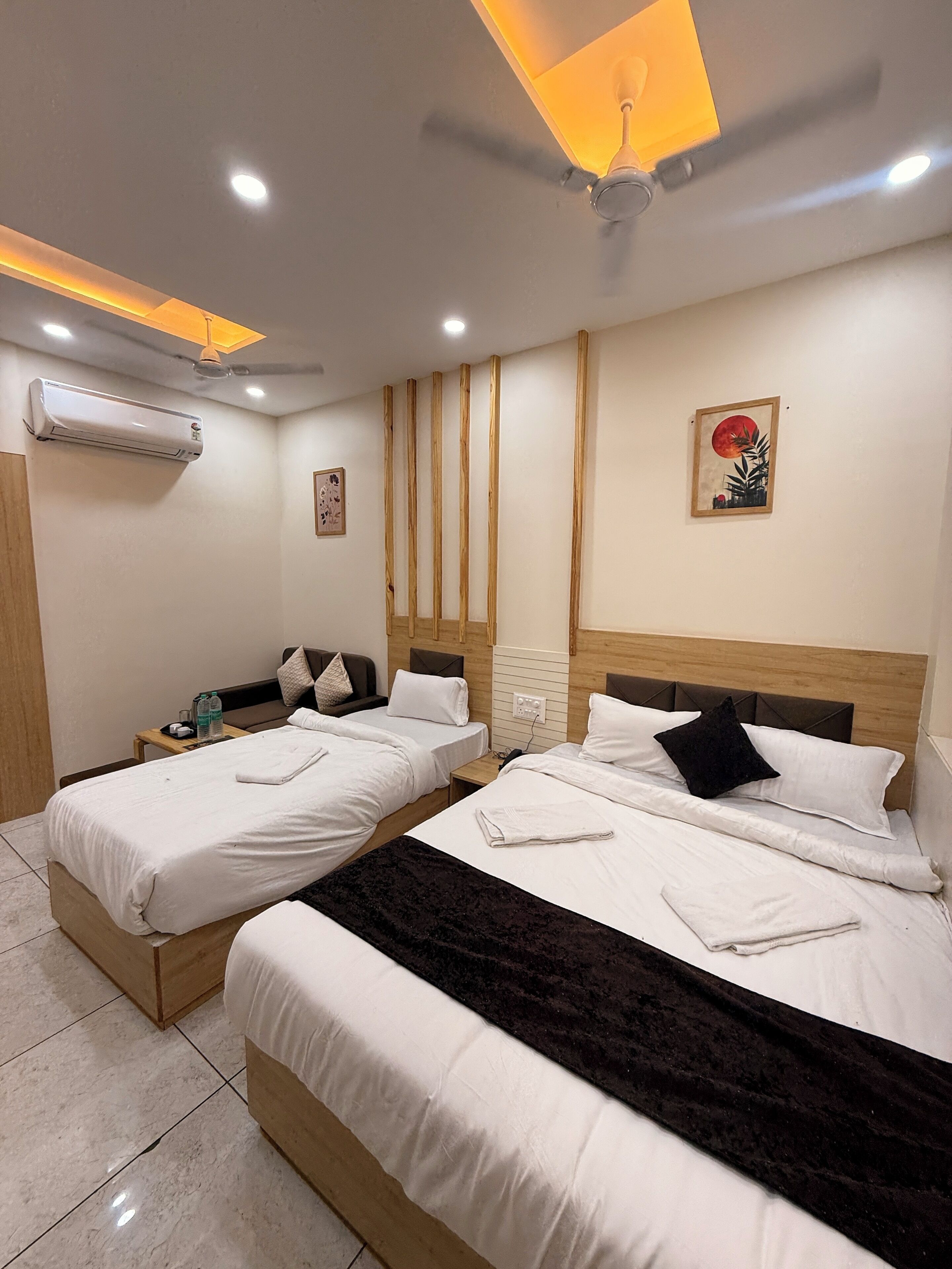 A hotel room with two beds, a ceiling fan, an air conditioner, and a painting on the wall.