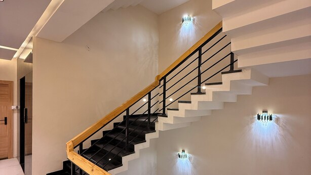 Una escalera moderna con barandillas de madera y rieles de metal negro, que conduce a un piso superior.