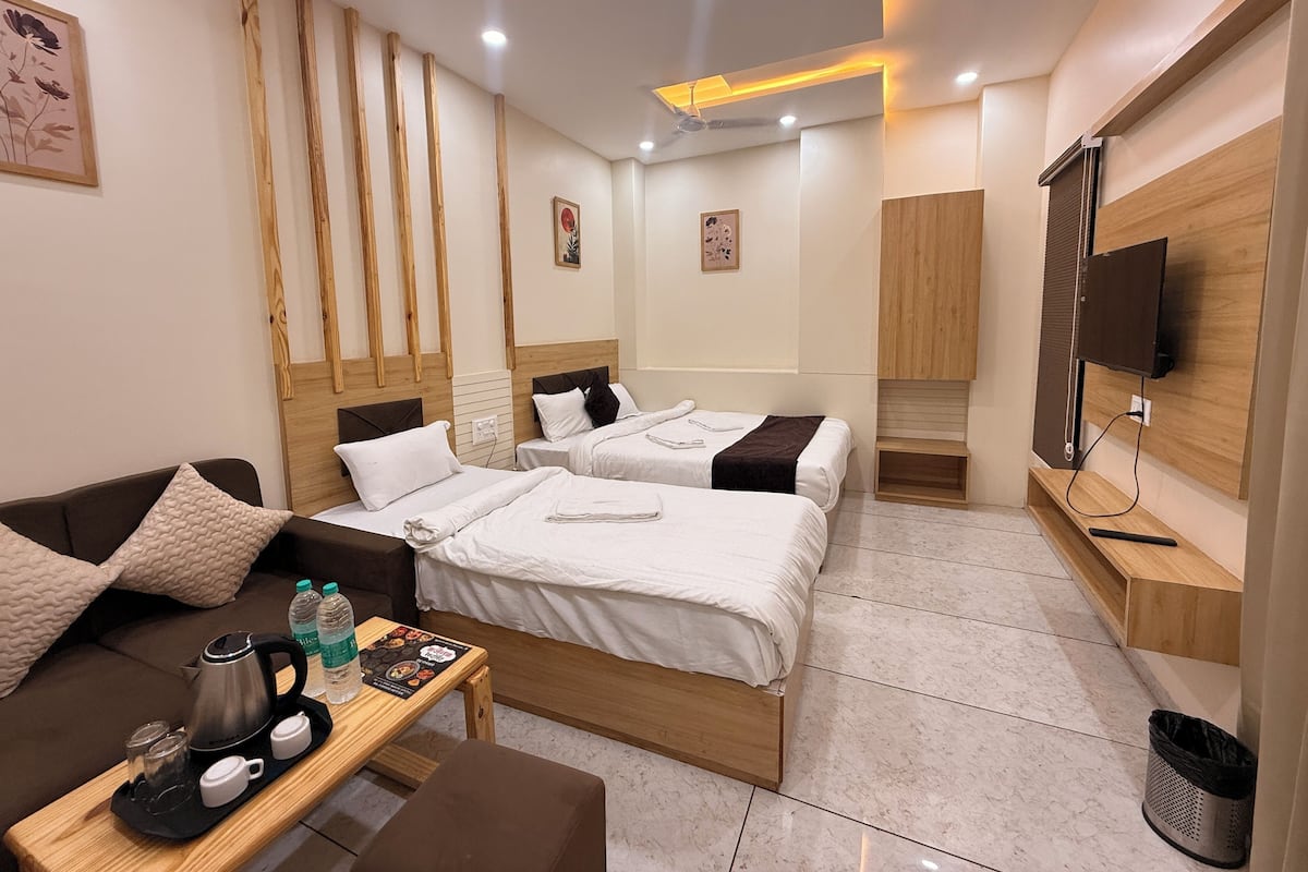 Quarto de hotel com duas camas, um sofá, uma mesa de centro com bandeja, uma televisão e um pequeno estante.
