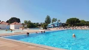 Una piscina con gente, un tobogán y sillones de descanso.