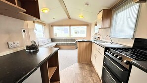 Une cuisine compacte équipée d’une cuisinière, d’un évier et d’un coin salon offrant une vue sur l’extérieur.