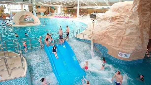 Un parc aquatique intérieur doté d’une grande piscine, d’un toboggan aquatique et d’une cascade artificielle en forme de rocher.