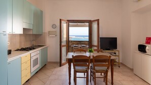 A compact kitchen with a dining area, a TV, and a view of the sea.