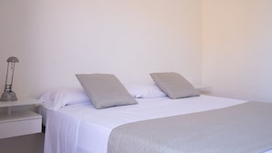 A neatly made bed with a white and gray bedspread, two pillows, and a bedside table with a lamp.