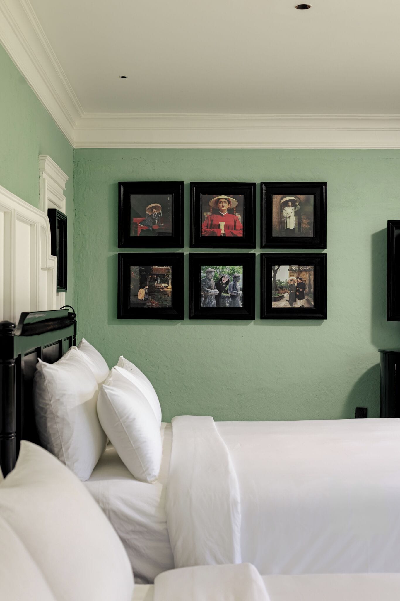 A room with two beds, a green wall, and six framed pictures.