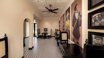 A hallway with black and white patterned flooring, a ceiling fan, framed artwork on the walls, and a dining area with tables and chairs.