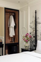 Una camera d'hotel con un armadio, un comodino con un vaso di fiori, un letto e un tavolino.