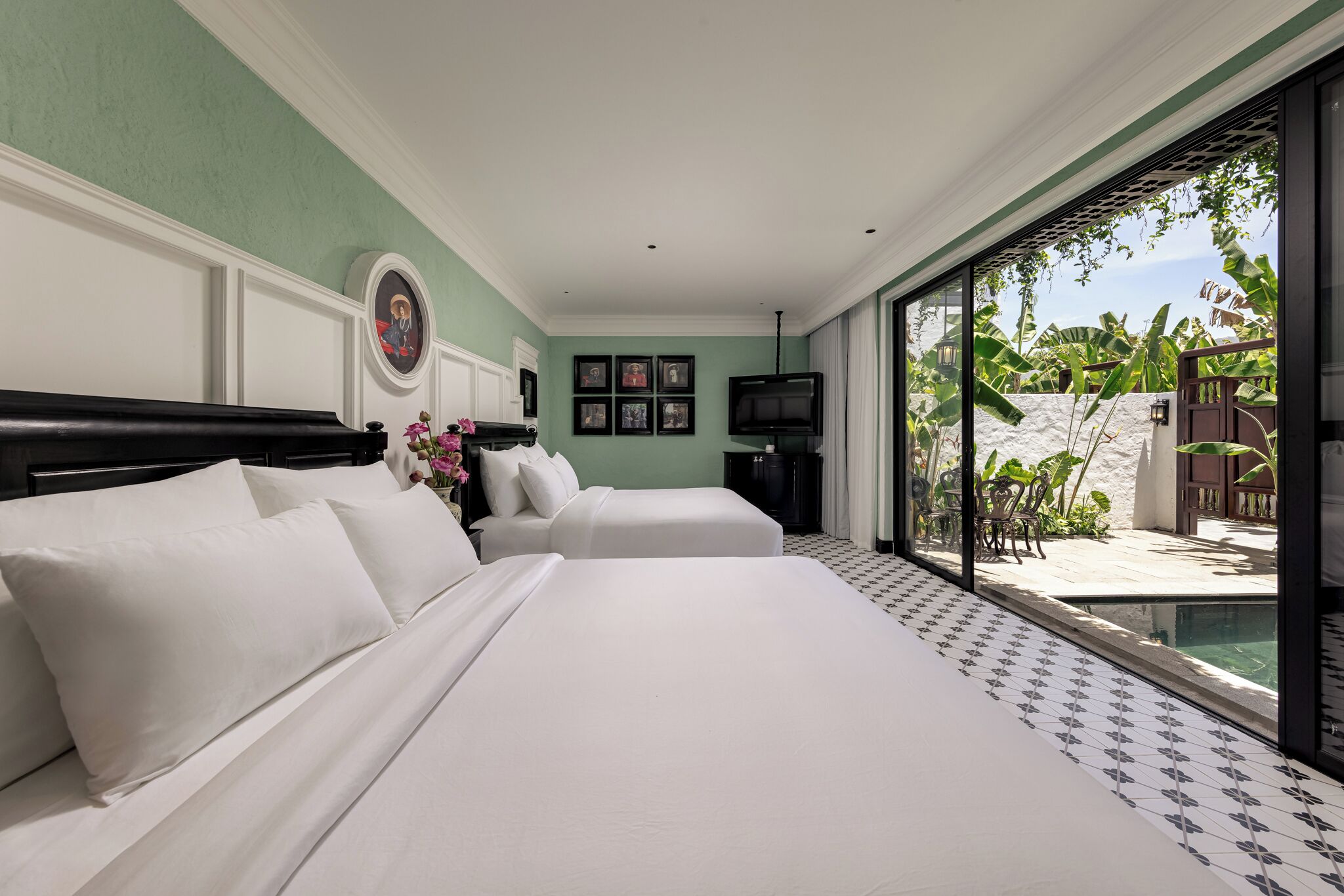 A hotel room with a large bed, two bedside tables, a television, and a view of a pool and outdoor area.