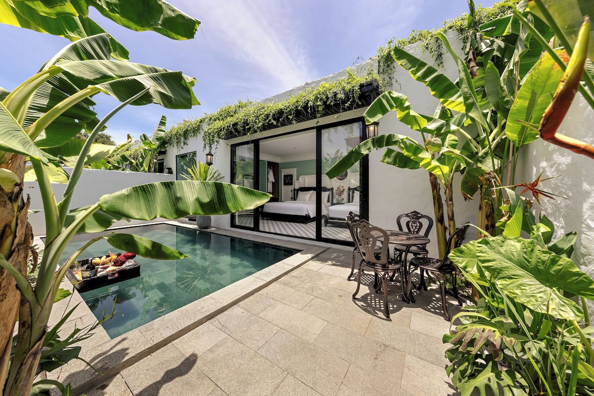 A modern outdoor pool area with a glass-enclosed room, surrounded by lush tropical plants.