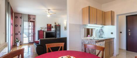 Eine moderne Küche mit Holzausstattung, ein Essbereich mit einem roten Tisch und ein Wohnzimmer mit einer Couch und Deckenventilator.