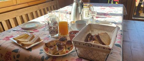 A wooden dining table with a floral tablecloth, plates of bread, a pitcher of orange juice, and a coffee pot.