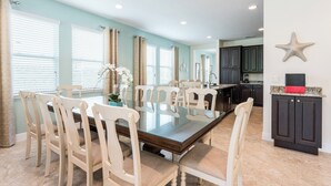 A spacious dining area with a large glass table surrounded by white chairs, a kitchen area with dark cabinets, and a decorative starfish on the wall. - Spacious 8-bedroom apartment with WiFi, fitness room in wonderful Kissimmee (Kissimmee)