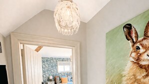 A room with a wooden floor, a white door leading to another room, a hanging light fixture, and a painting of a rabbit on the wall. - The Old Ropery at Mill Cottage - Unwind where ropes once twined (Ollerton)