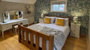 A bedroom with a wooden bed, a vanity with a mirror, a dresser, a window with a view, and a ceiling lamp. - The Old Ropery at Mill Cottage - Unwind where ropes once twined (Ollerton)