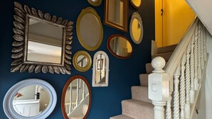 A staircase with beige carpeted steps and white balusters, leading to a room with a dark blue wall adorned with various mirrors. - The Old Ropery at Mill Cottage - Unwind where ropes once twined (Ollerton)
