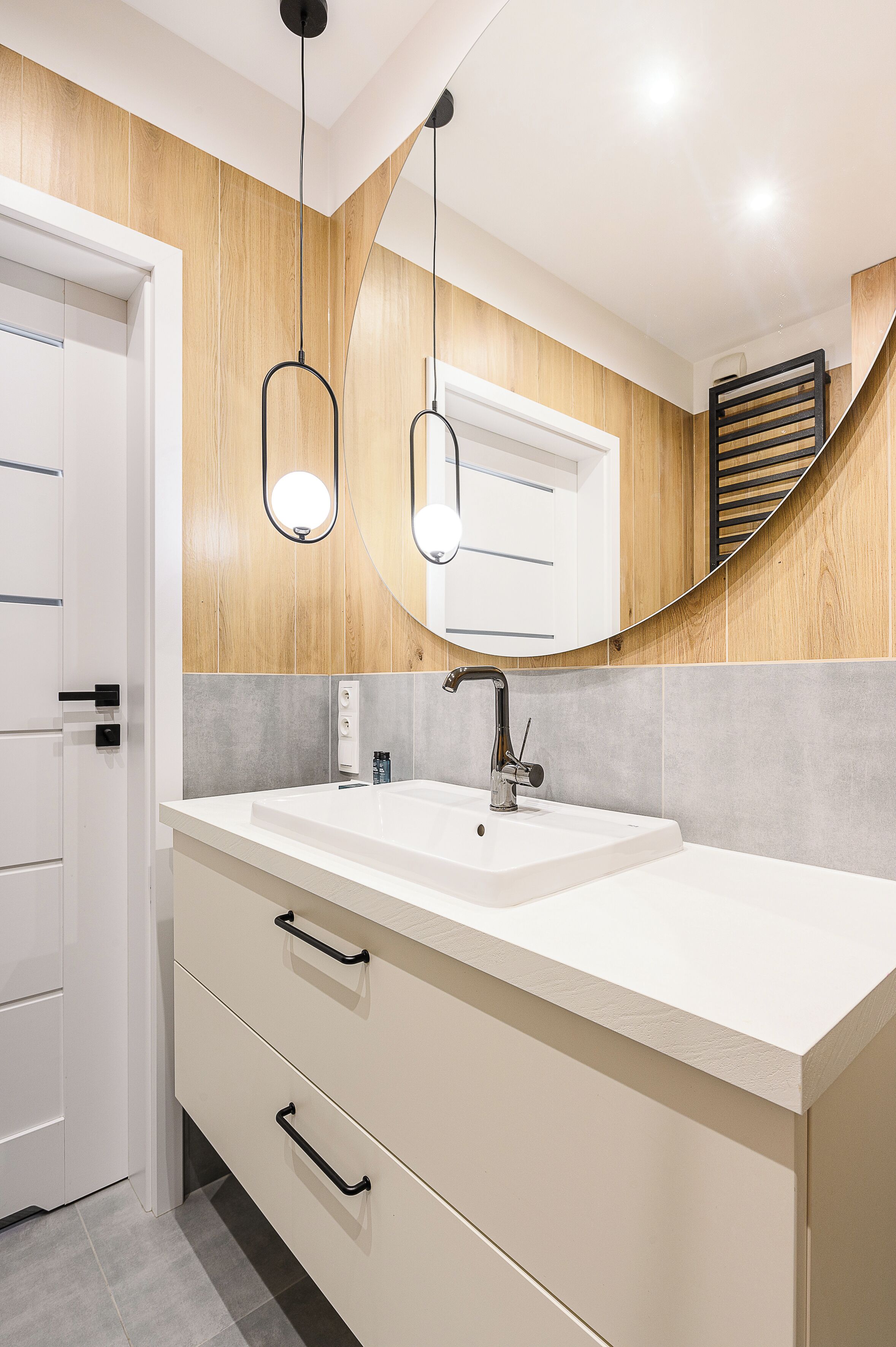 A bathroom with a white sink, two black handles, a mirror, and wooden paneling.