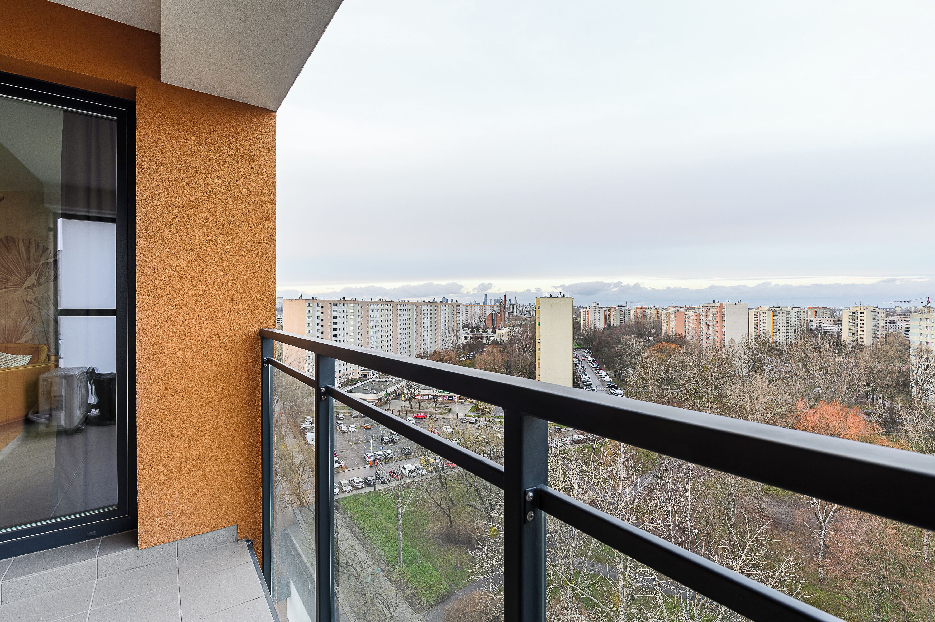 A balcony with a view of a cityscape, including high-rise buildings and a distant mountain range.