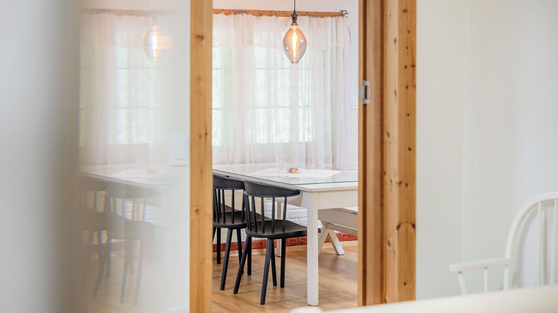A dining area with a table and chairs, a hanging light fixture, and a view through a doorway.